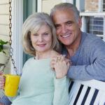 Elderly couple smiling on porch looking at camera