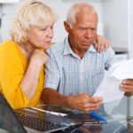 Worried mature couple with documents near laptop in home